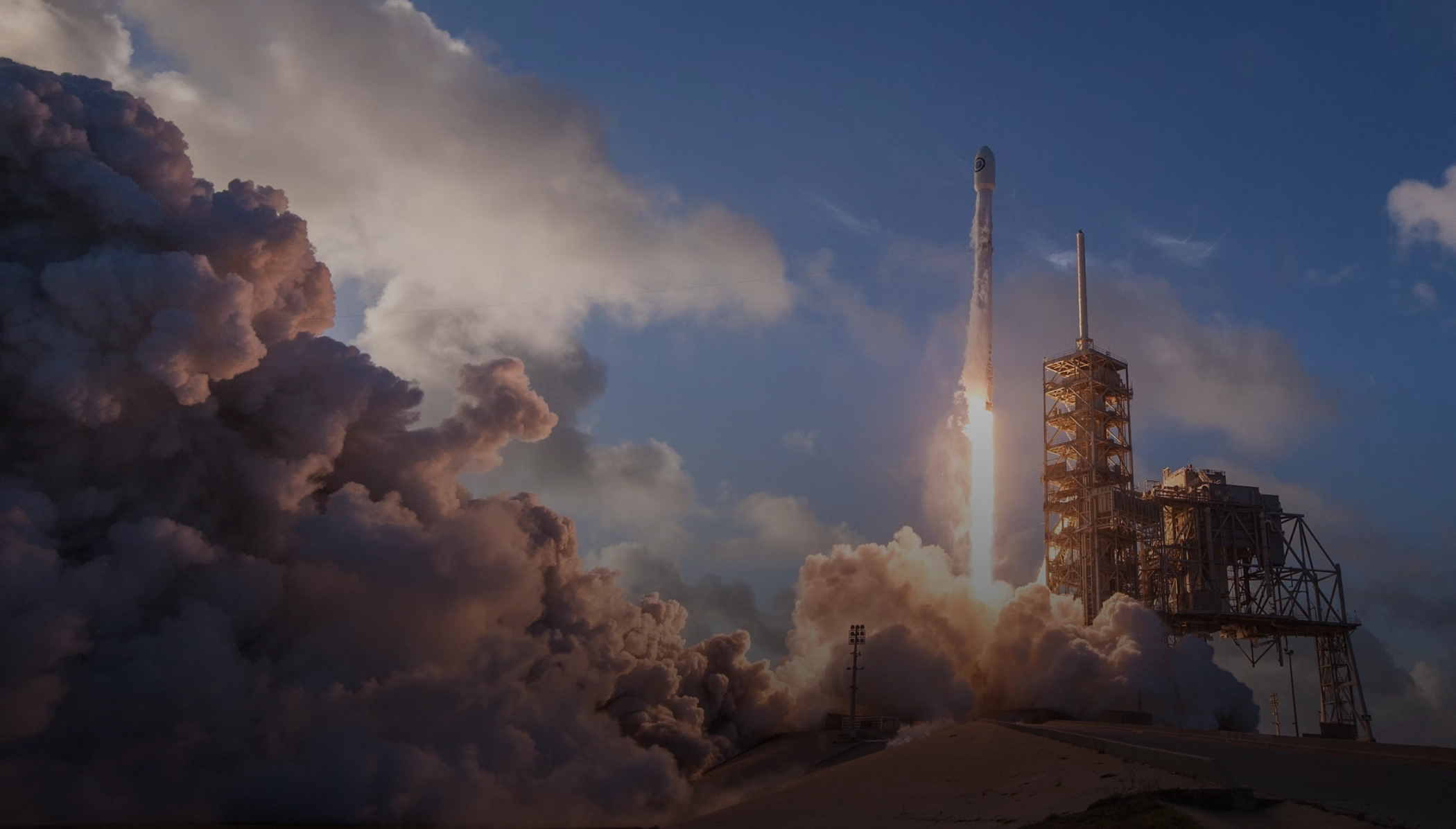 A rocket launches above an industrial launch tower